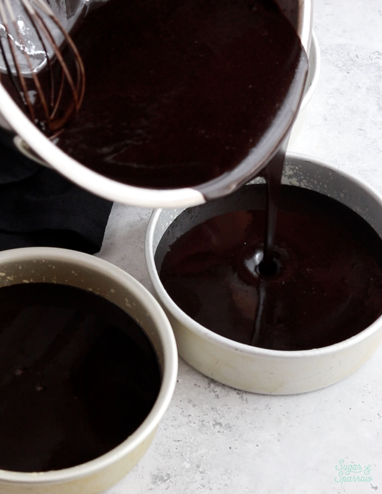 pouring black velvet cake batter into cake pans