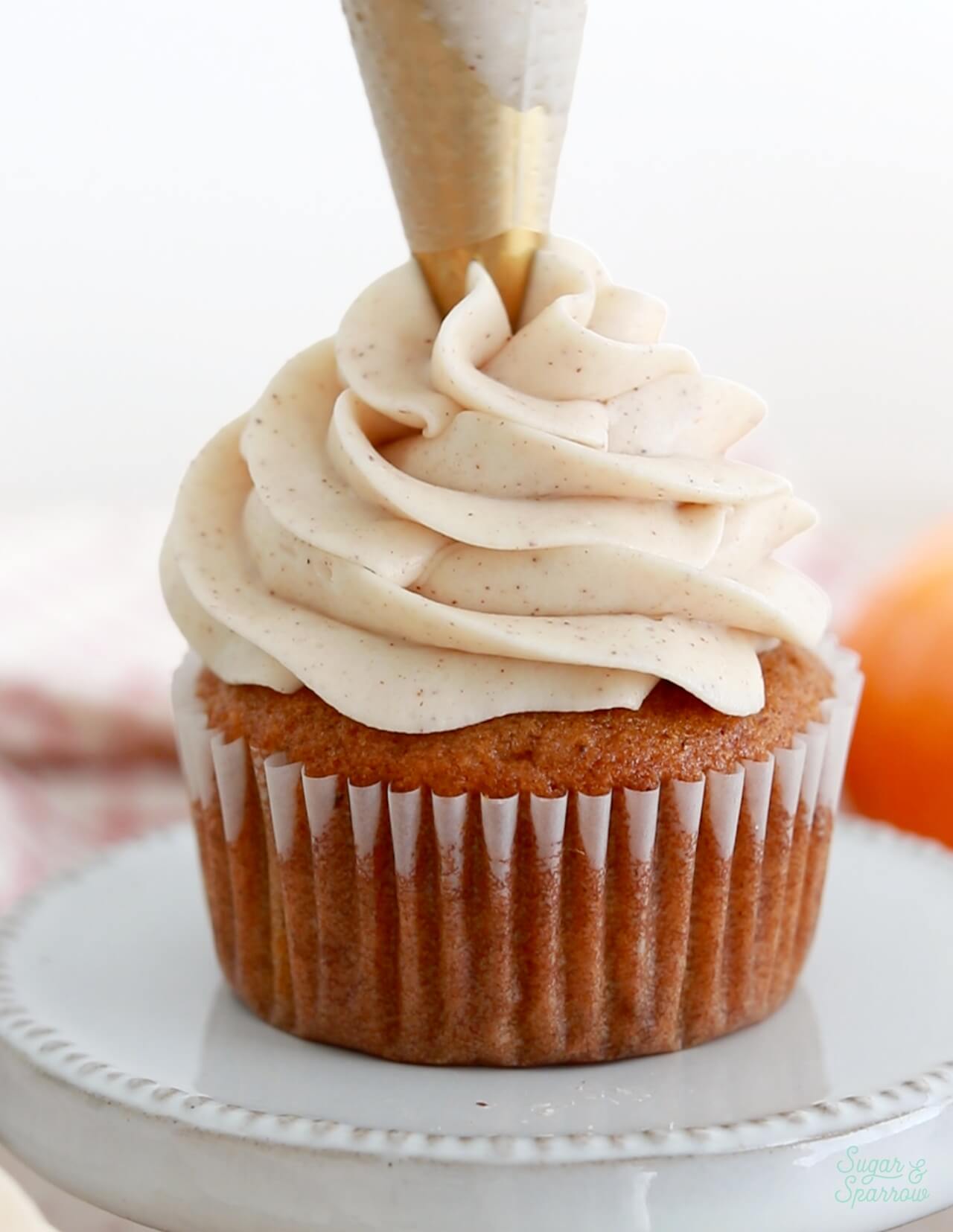 piping a swirl of cream cheese frosting onto pumpkin cupcake