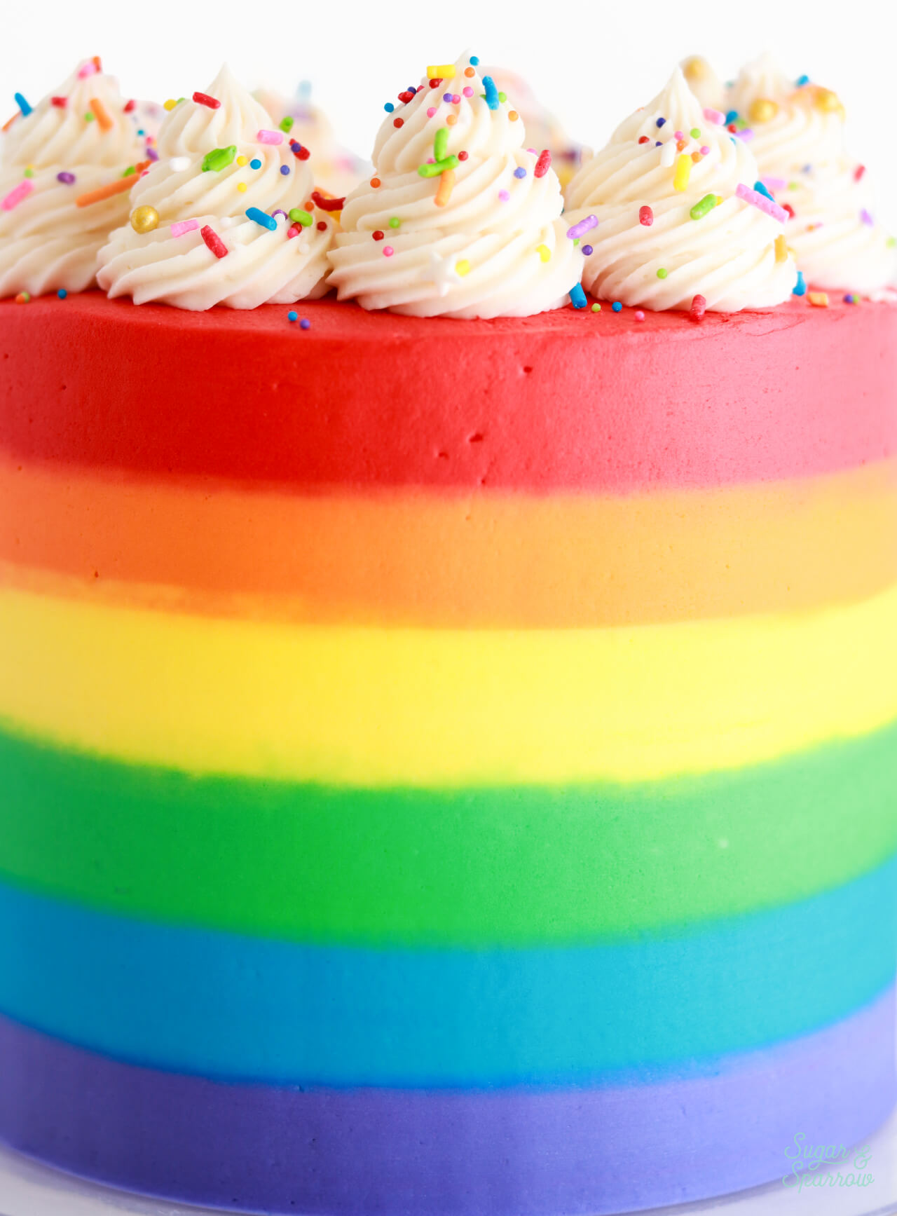 rainbow striped buttercream cake with white swirls on top