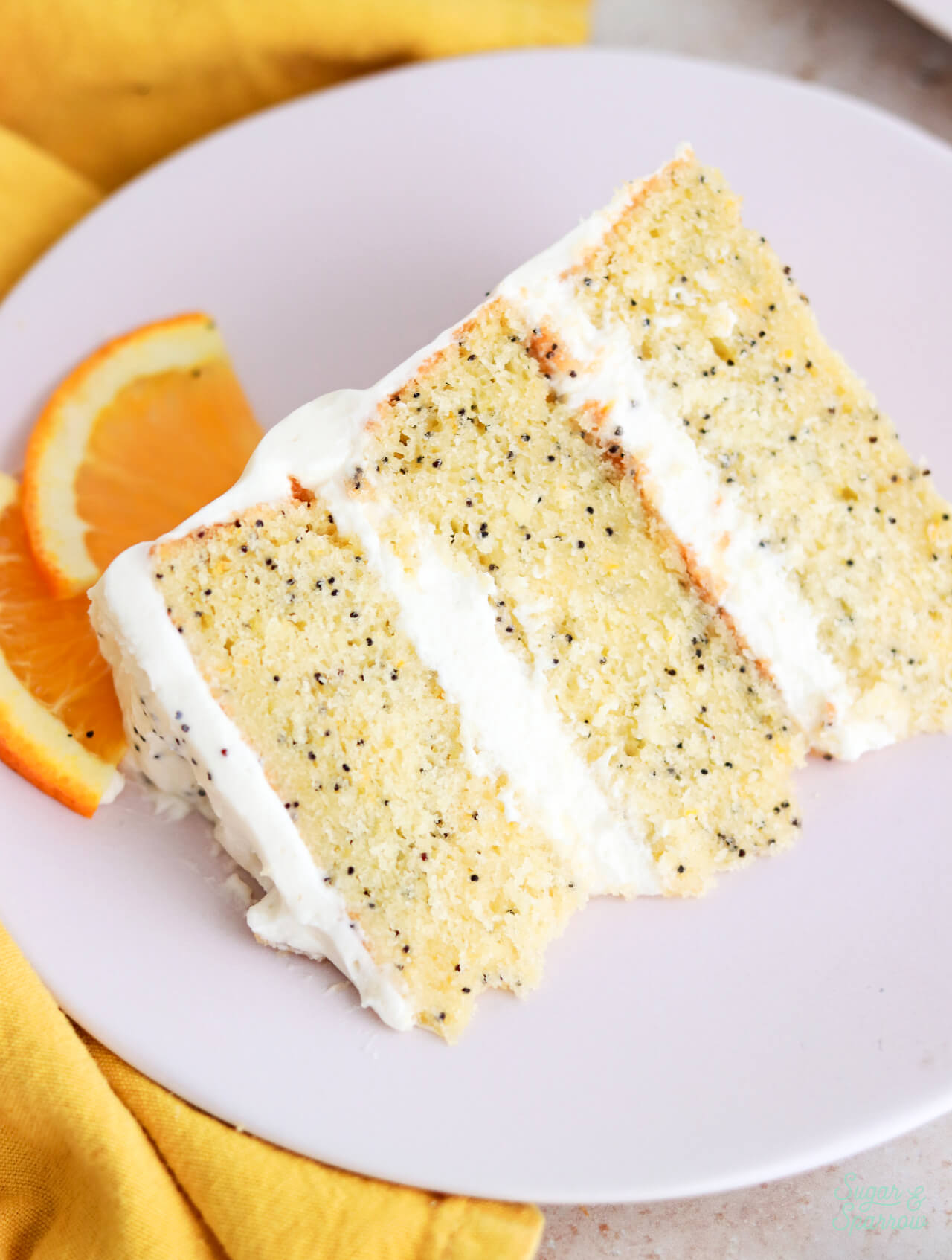 slice of orange poppyseed cake with mascarpone frosting on a pink plate