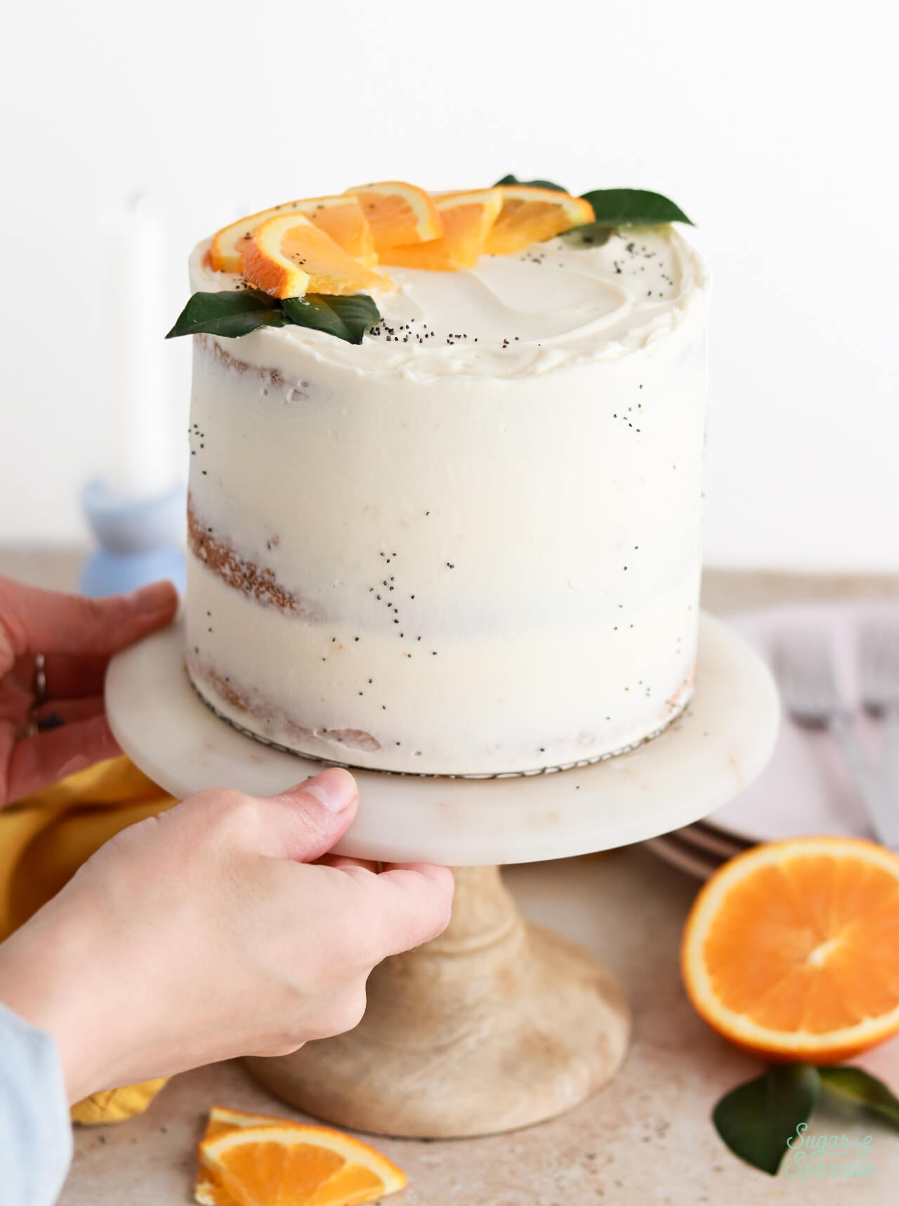 orange poppyseed semi-naked cake with mascarpone frosting on a rustic cake stand