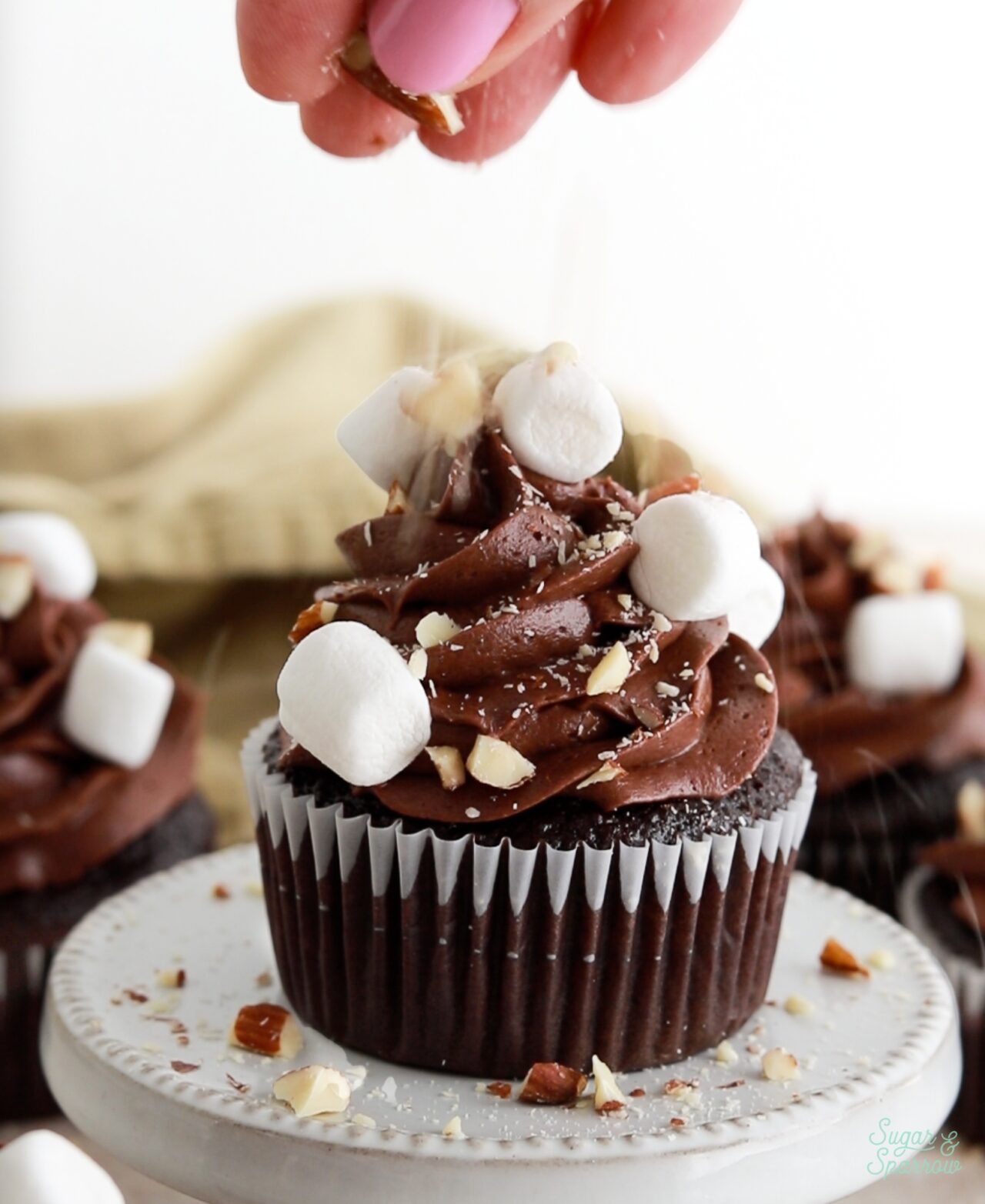 topping a chocolate cupcake with chopped almonds and mini marshmallows