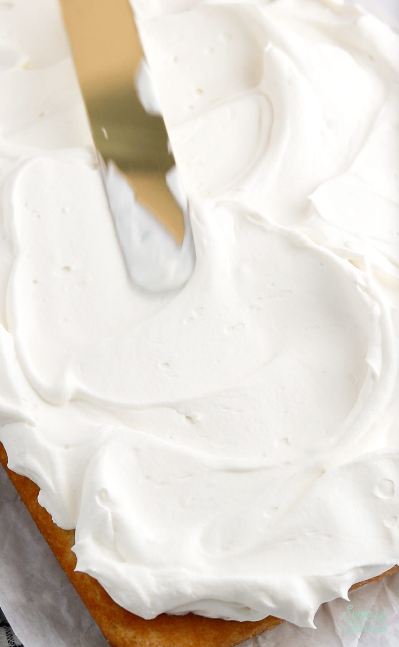 frosting a vanilla sheet cake with whipped cream frosting